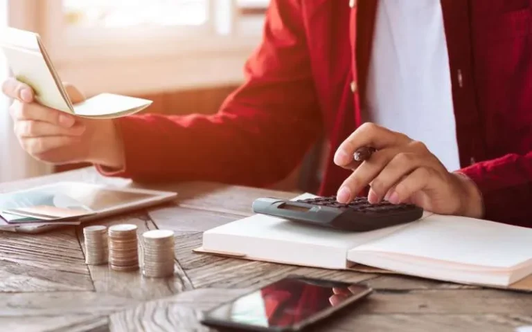 Mãos contando cédulas de dinheiro ao lado de calculadora e caderno
