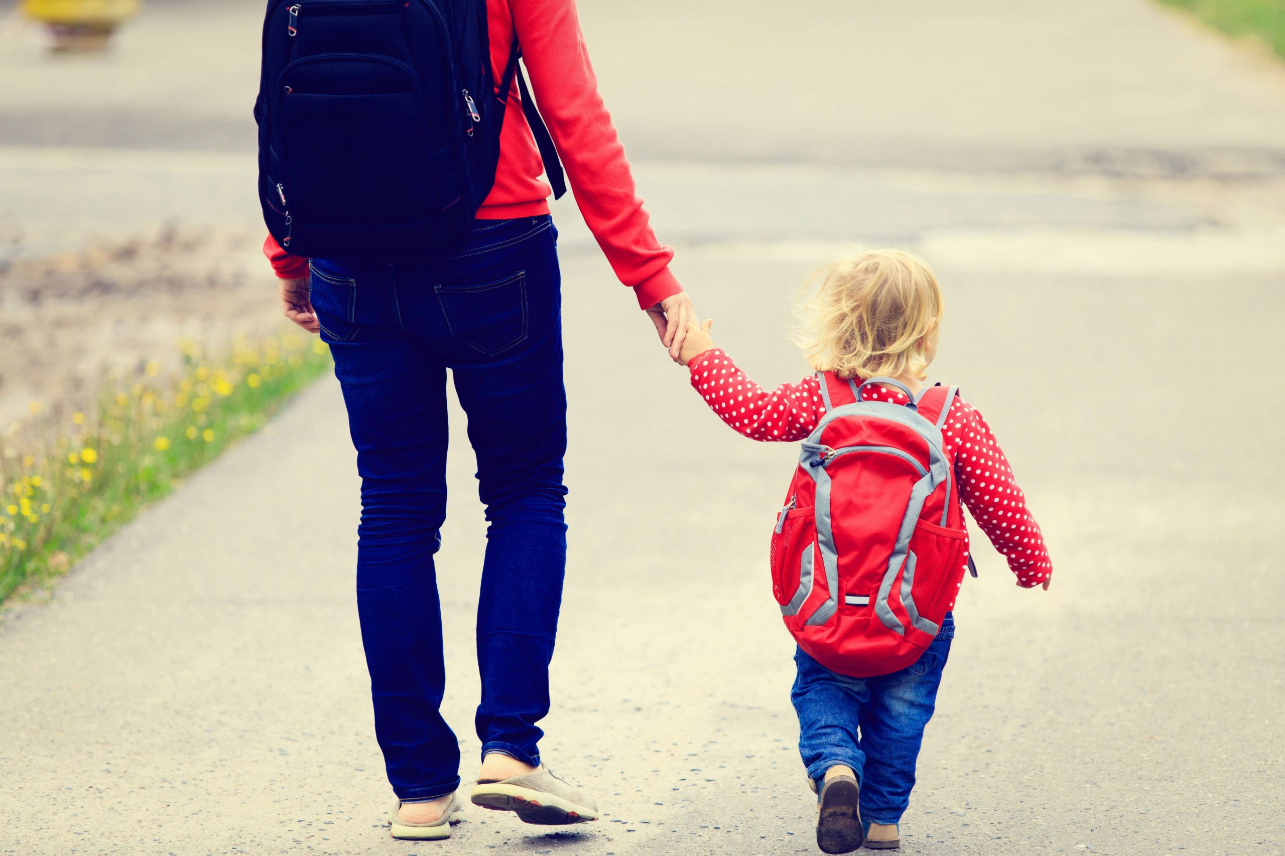 Mother holding hand of little daughter with backpack