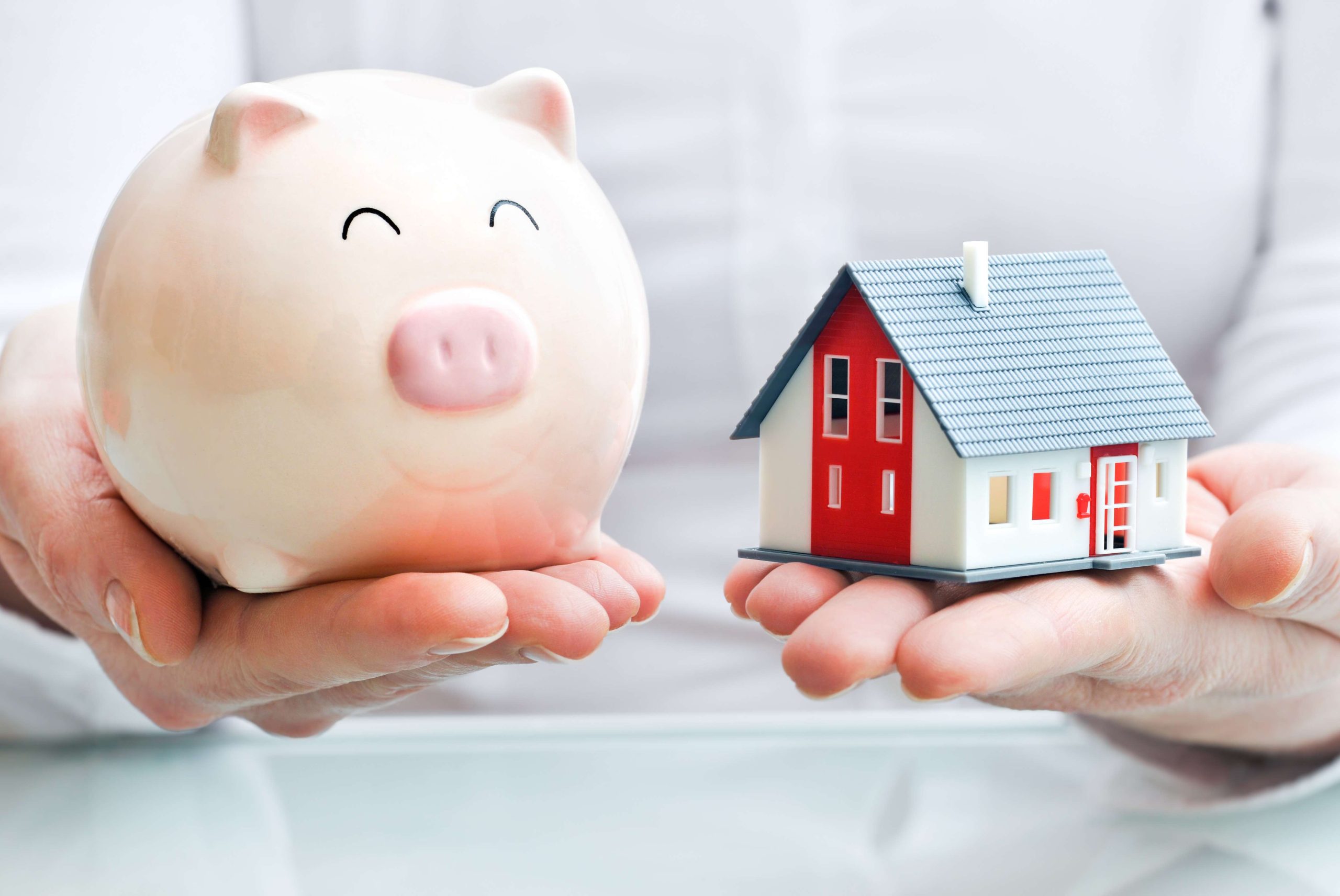 Hands holding a  piggy bank and a house model